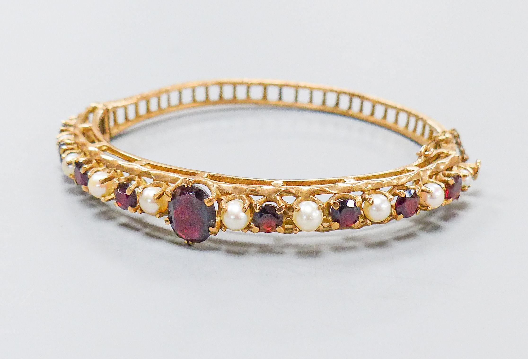 A 9ct gold, garnet and cultured pearl set hinged bracelet, gross weight 16.1 grams.